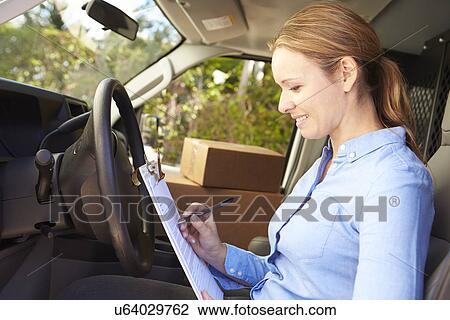 Stock Image - Female Delivery Driver Sitting In Van Filling Out Paperwork. Fotosearch