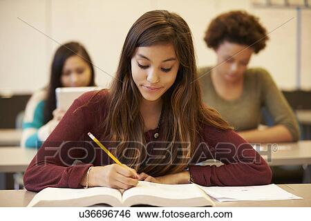Stock Photograph - Female High School Student Studying At Desk In Classroom. Fotosearch