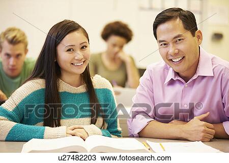 Stock Image - Female High School Student With Teacher Studying At Desk. Fotosearch