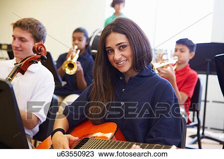Stock Image - Female Pupil Playing Guitar In High School Orchestra. Fotosearch