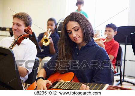 Stock Image - Female Pupil Playing Guitar In High School Orchestra. Fotosearch