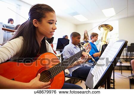Stock Photograph - Female Pupil Playing Guitar In High School Orchestra. Fotosearch
