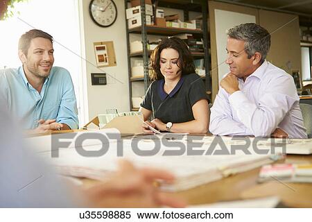 Stock Photography - Four Architects Sitting Around Table Having Meeting. Fotosearch