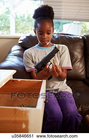 Stock Image - Girl Playing With Parent's Gun She Has Found At Home. Fotosearch