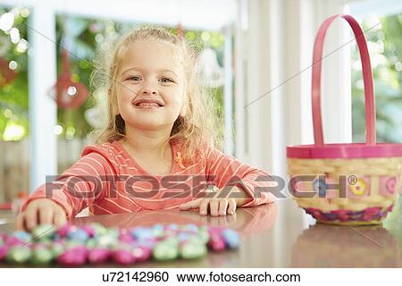 Stock Image - Girl With Chocolate Easter Eggs And Basket At Home. Fotosearch