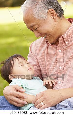 Stock Photo - Grandfather Holding Sleeping Grandson In Park. Fotosearch