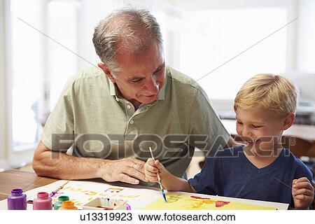 Stock Image - Grandfather Painting Picture With Grandson At Home. Fotosearch