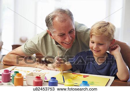 Stock Image - Grandfather Painting Picture With Grandson At Home. Fotosearch