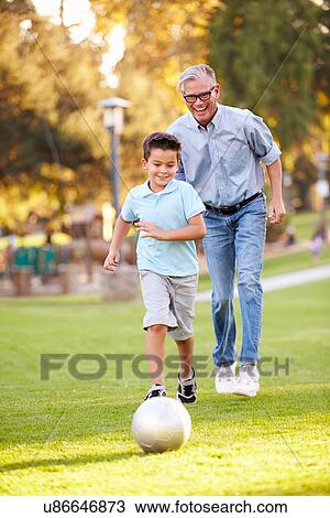 Stock Image - Grandfather Playing Football With Grandson In Park. Fotosearch