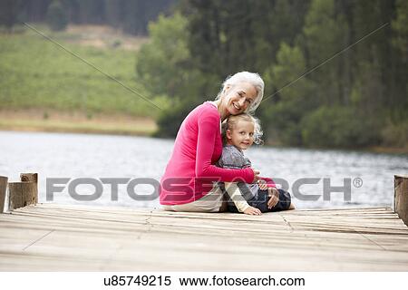 Stock Photography - Grandmother and granddaughter sitting on a jetty. Fotosearch