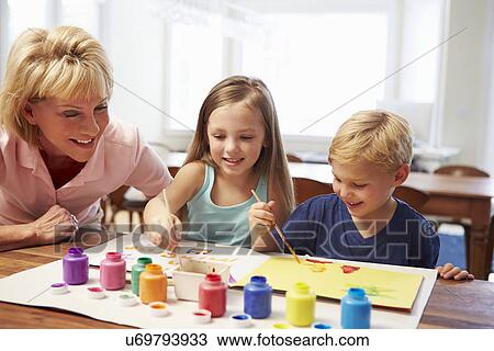 Stock Image - Grandmother Painting Picture With Grandchildren At Home. Fotosearch