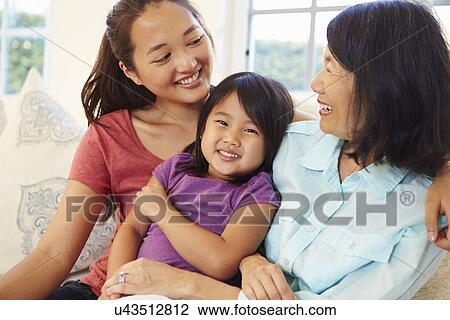 Stock Image - Grandmother Playing On Sofa With Granddaughter And Daughter. Fotosearch