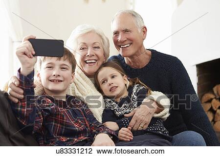 Stock Image - Grandparents And Grandchildren Sitting On Sofa Taking Selfie. Fotosearch