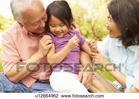 Stock Image - Grandparents Cuddling Granddaughter In Park. Fotosearch