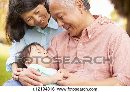 Stock Photograph - Grandparents Holding Sleeping Grandson In Park. Fotosearch