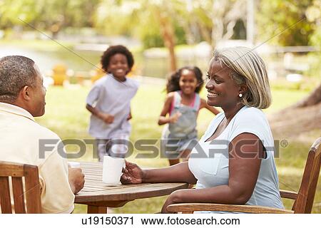 Stock Image - Grandparents Relaxing Whilst Grandchildren Play In Garden . Fotosearch