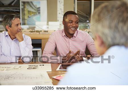 Stock Photography - Group Of Architects Sitting Around Table Having Meeting. Fotosearch