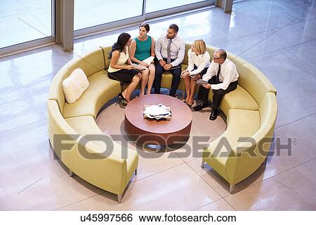 Stock Photograph - Group Of Businesspeople Having Meeting In Office Lobby. Fotosearch