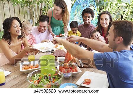 Stock Image - Group Of Families Enjoying Outdoor Meal At Home. Fotosearch