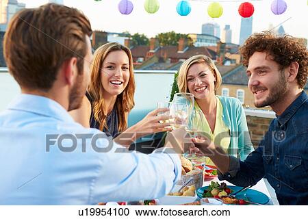 Stock Image - Group Of Friends Eating Meal On Rooftop Terrace. Fotosearch