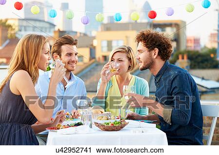 Stock Image - Group Of Friends Eating Meal On Rooftop Terrace. Fotosearch