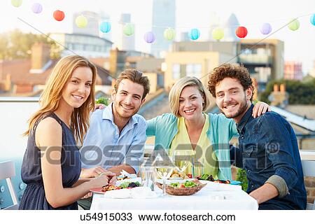Stock Image - Group Of Friends Eating Meal On Rooftop Terrace. Fotosearch