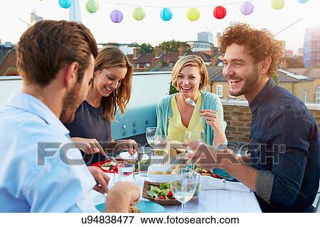 Stock Photo - Group Of Friends Eating Meal On Rooftop Terrace. Fotosearch