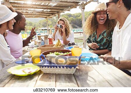 Stock Photo - Group Of Friends Enjoying Lunch And Taking Photographs . Fotosearch