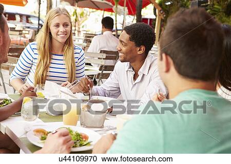 Stock Image - Group Of Friends Enjoying Lunch In Outdoor Restaurant. Fotosearch