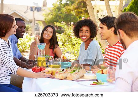 Stock Image - Group Of Friends Enjoying Meal At Outdoor Party In Back Yard. Fotosearch