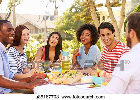 Stock Image - Group Of Friends Enjoying Meal At Outdoor Party In Back Yard. Fotosearch