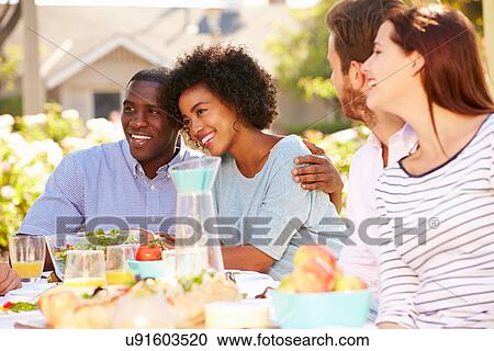 Stock Image - Group Of Friends Enjoying Meal At Outdoor Party In Back Yard. Fotosearch
