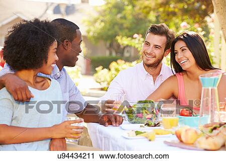 Stock Image - Group Of Friends Enjoying Meal At Outdoor Party In Back Yard. Fotosearch