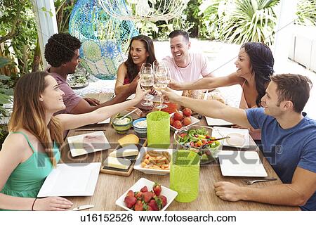 Stock Photograph - Group Of Friends Enjoying Meal Outdoors At Home. Fotosearch