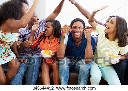 Stock Image - Group Of Friends Sitting On Sofa Watching TV Together. Fotosearch