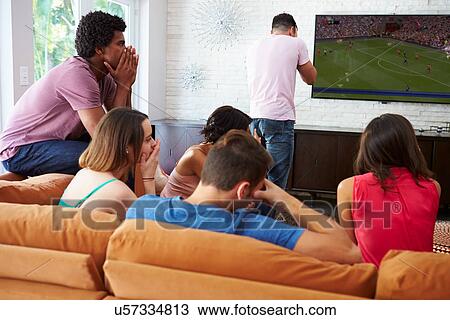 Stock Image - Group Of Friends Sitting On Sofa Watching Soccer Together. Fotosearch