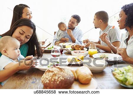Stock Photo - Group Of Friends With Babies Enjoying Meal At Home Together. Fotosearch