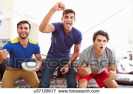 Stock Photo - Group Of Men Sitting On Sofa Watching Sport Together. Fotosearch