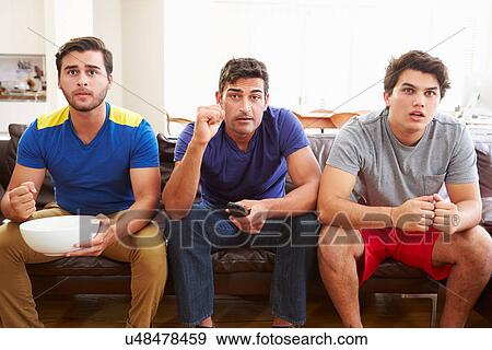 Stock Photo - Group Of Men Sitting On Sofa Watching Sport Together. Fotosearch