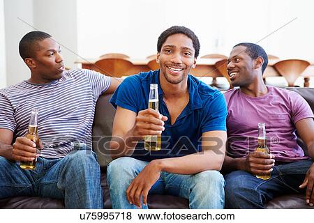 Stock Photo - Group Of Men Sitting On Sofa Watching TV Together. Fotosearch
