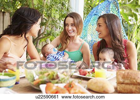Stock Image - Group Of Mothers With Babies Enjoying Outdoor Meal At Home. Fotosearch