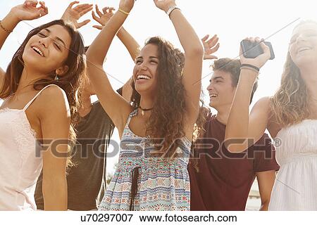 Stock Photo - Group Of Teenage Friends Dancing Outdoors Against Sun. Fotosearch