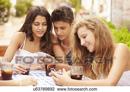 Stock Image - Group Of Teenage Friends Using Mobile Phone Sitting At Cafe . Fotosearch