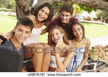Stock Photo - Group Of Teenagers Sitting On Bench Taking Selfie In Park. Fotosearch
