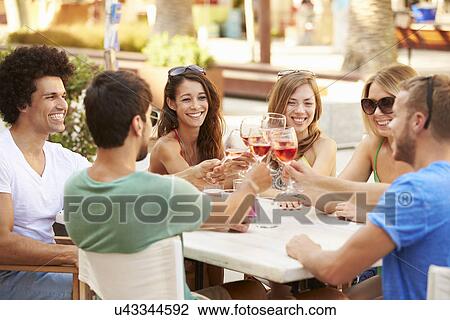 Stock Image - Group Of Young Friends Enjoying Meal In Outdoor Restaurant. Fotosearch