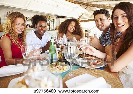 Stock Image - Group Of Young Friends Enjoying Meal In Outdoor Restaurant. Fotosearch