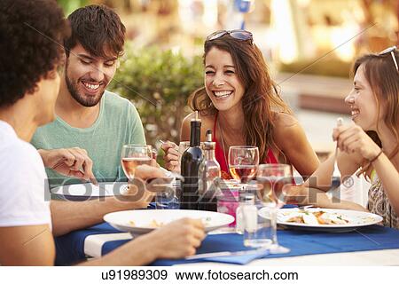 Stock Photo - Group Of Young Friends Enjoying Meal In Outdoor Restaurant. Fotosearch