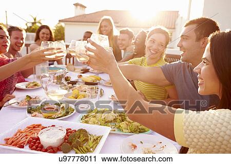 Stock Image - Group Of Young People Enjoying Outdoor Summer Meal. Fotosearch