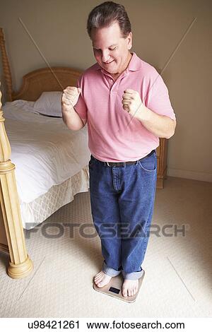 Happy Overweight Man Standing On Scales In Bedroom View Large Photo Image Stock Image - Happy Overweight Man Standing On Scales In Bedroom. Fotosearch