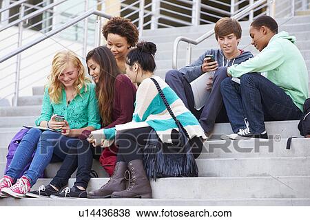 Stock Photo - High School Students Sitting Outside Building With Phones. Fotosearch